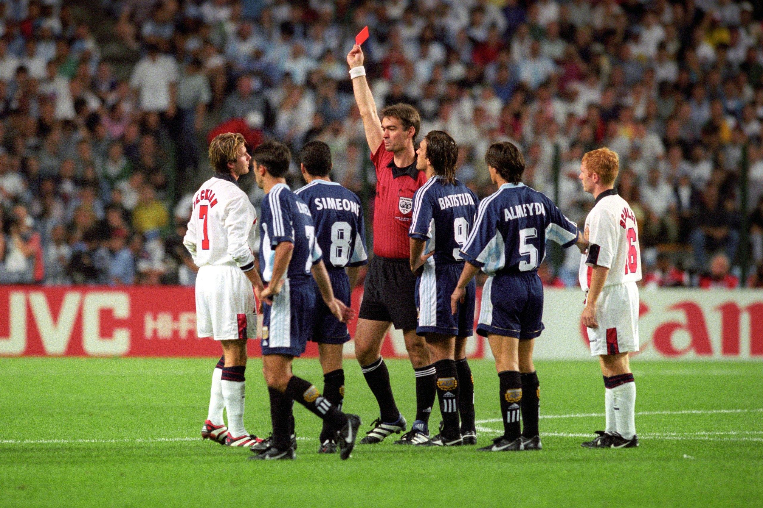 Referee Kim Milton Nielsen shows the red card to David Beckham while being surrounded by players