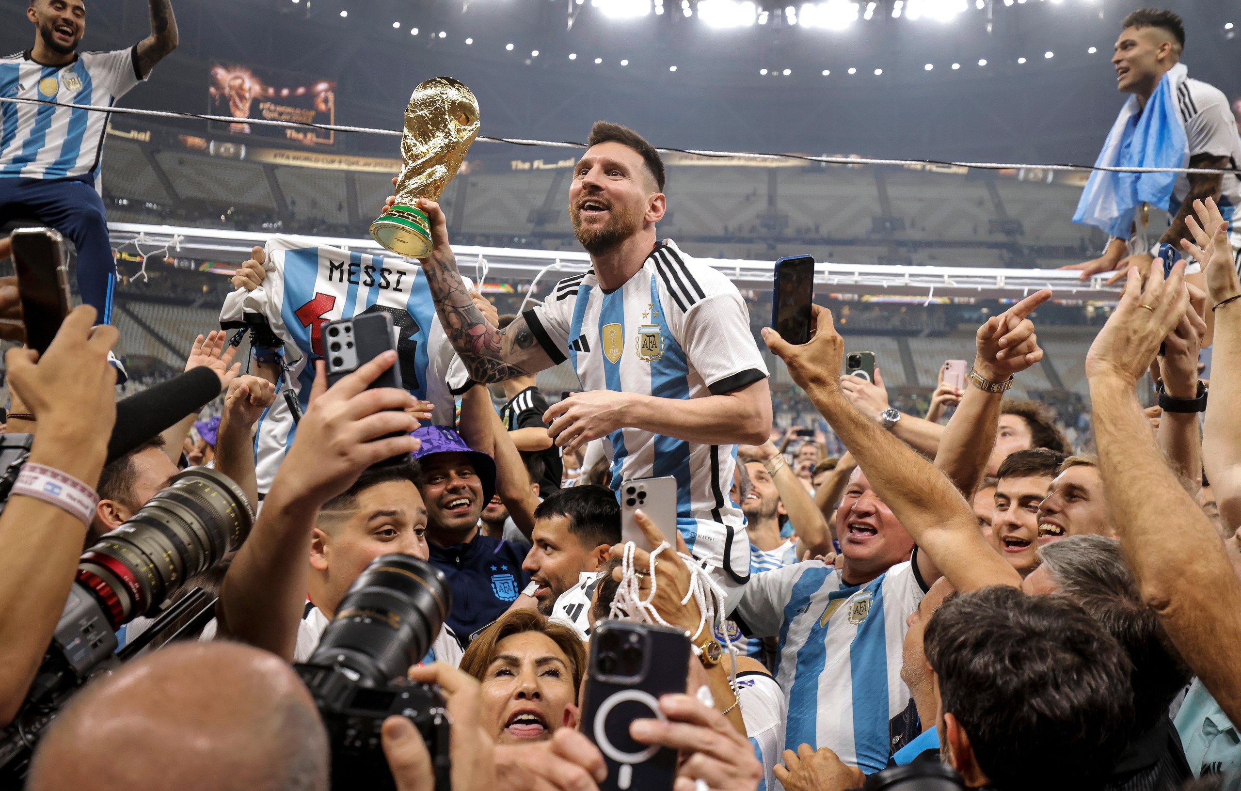 Messi is held aloft by teammates with the World Cup trophy in his hand as he is surrounded by photographers